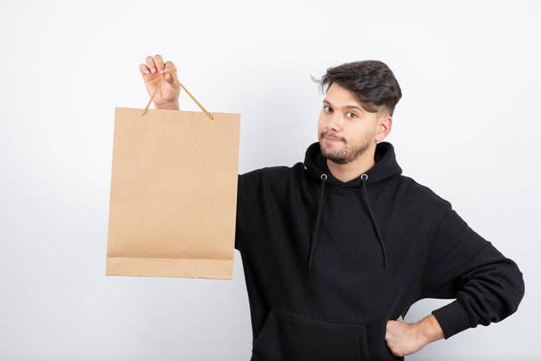Image of handsome man in black hoodie holding craft bag. High quality photo - Foto, afbeelding