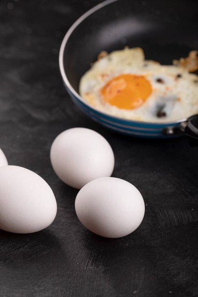 Kızartma tavasında nefis kızarmış yumurta ve siyah yüzeyde çiğ beyaz yumurta. Yüksek kalite fotoğraf - Fotoğraf, Görsel