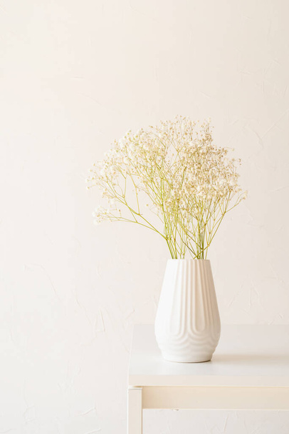 Белые цыганские цветы в белой вазе на столе, минимальный стиль, пространство для копирования - Фото, изображение