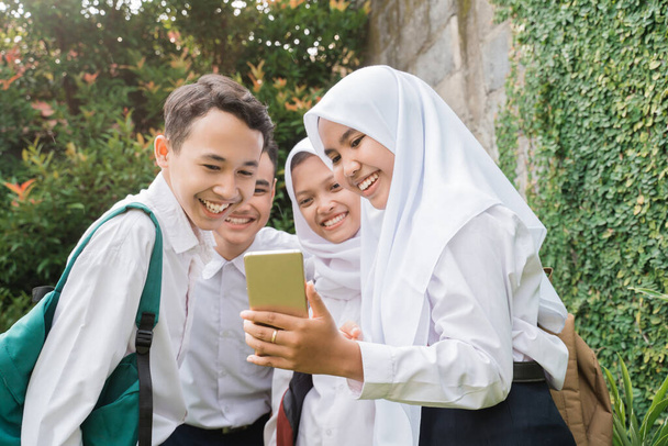 four teenagers in junior high school uniforms using and looking at cellphones - Φωτογραφία, εικόνα