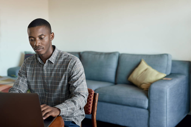 Młody afrykański biznesmen korzystający z laptopa podczas pracy zdalnej z domu przy stole w salonie - Zdjęcie, obraz