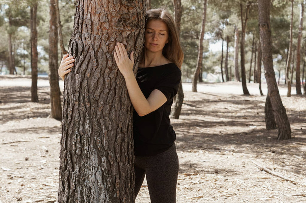 A middle-aged sensual Caucasian woman hugging a tree and loving nature at a park - Φωτογραφία, εικόνα