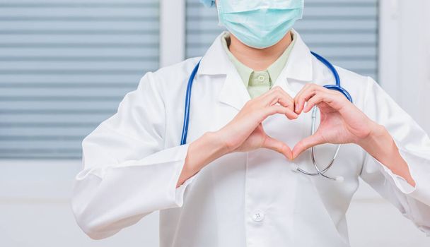 Closeup of doctor woman wearing white coat standing making heart finger shape, Doctor's hand sign, Healthy medical heart coronavirus concept - 写真・画像