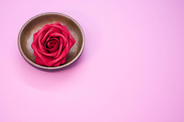 A closeup shot of a red rose in a wooden bowl on a pink background - Photo, Image