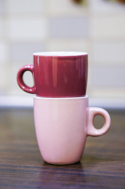 A closeup of the two pink colored ceramic cups on each other on the wooden surface - Foto, Imagen