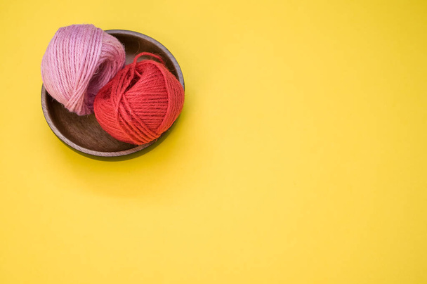 A top view of red and pink yarns for knitting in a wooden bowl on a yellow background - Foto, Bild