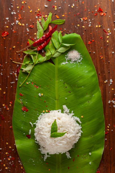 Lähikuva Intian keitettyä riisiä yli banaanin tuoreen vihreän lehden. Koristeltu curry-patta lehdet ja punainen chili paperia ja suolaa. - Valokuva, kuva