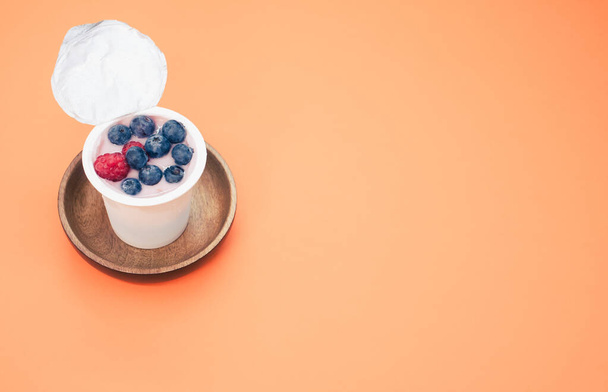 A berry yogurt in a plastic cup on an orange background - Zdjęcie, obraz