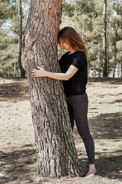 A middle-aged sensual Caucasian woman hugging a tree and loving nature at a park - Photo, Image