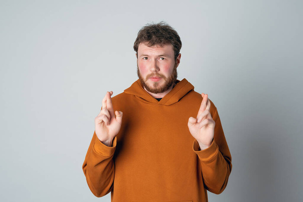 Worried redhead bearded handsome young man cross fingers and praying, frowning nervous, looking at camera with hopeful begging stare, standing over gray background - Fotografie, Obrázek