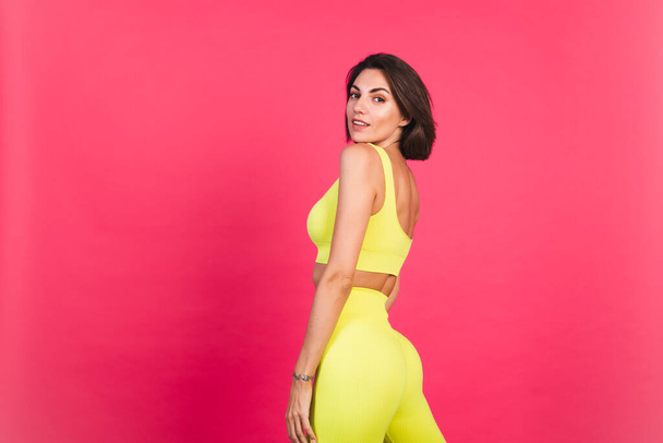 Krásná fit žena ve žluté jasně padnoucí sportovní oblečení na růžovém pozadí šťastný pohyb vzrušený perfektní tělo fitness motivace - Fotografie, Obrázek