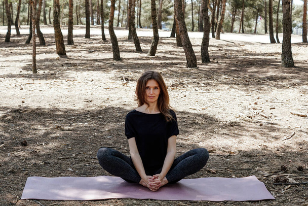 A middle-aged female in sportswear meditating in a park - Photo, image