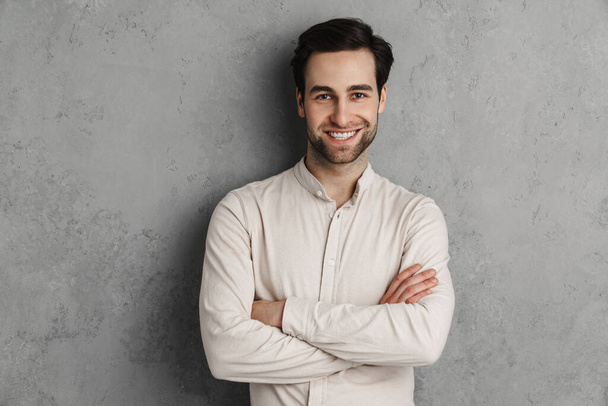 Joyful handsome guy smiling and looking at camera isolated over grey wall - Foto, imagen