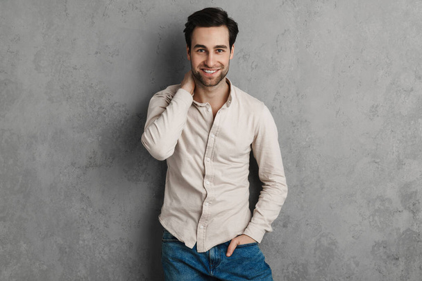 Joyful handsome guy smiling and looking at camera isolated over grey wall - Фото, изображение