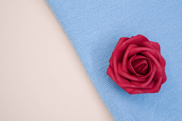 Ένα κοντινό πλάνο του διακοσμητικού τεχνητού κόκκινου τριαντάφυλλου στο μπλε ύφασμα - Φωτογραφία, εικόνα