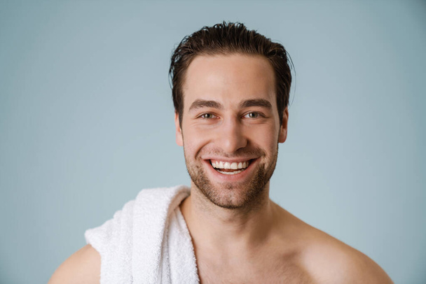Šťastná brunetka vousatý tričko muž s ručníkem přes modrou zeď - Fotografie, Obrázek