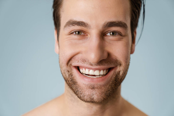 Close up of a smiling brunette shirtless man with stubble over blue background - Foto, Imagen