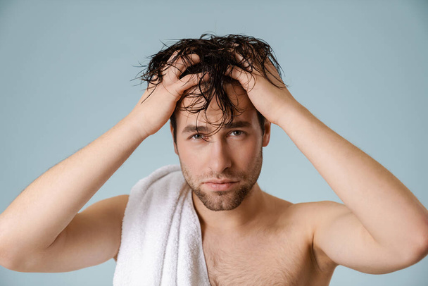 Shirtless white man touching his hair and looking at camera isolated over blue wall - Foto, afbeelding