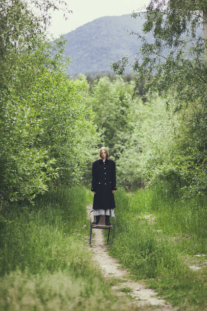 дівчина в пальто, що стоїть на стільці на фоні природи
 - Фото, зображення