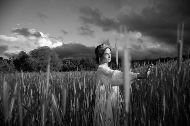 Monochrome Aufnahme einer schönen Frau, die tagsüber auf einem Feld spaziert, romantische Stimmung - Foto, Bild