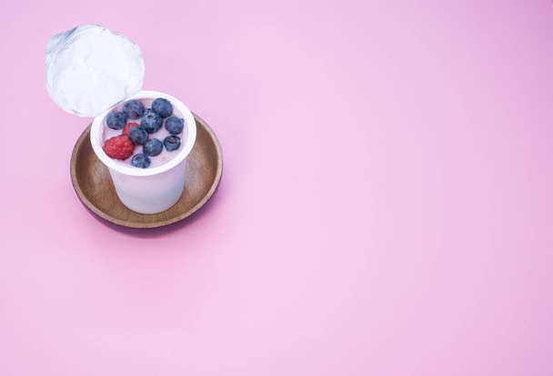 A top view of a berry yogurt in a plastic cup on a pink background - Zdjęcie, obraz