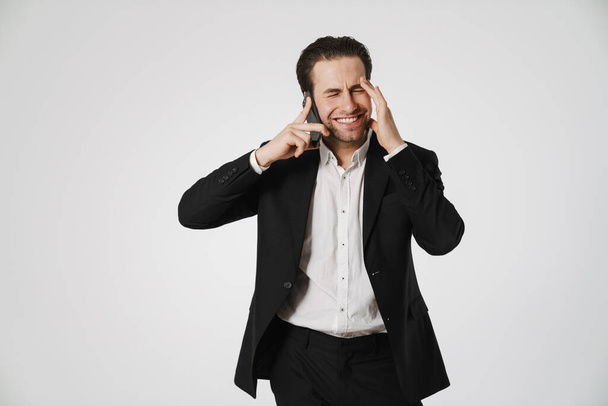 Unshaven brunette man in jacket smiling while talking on cellphone isolated over white background - Фото, изображение