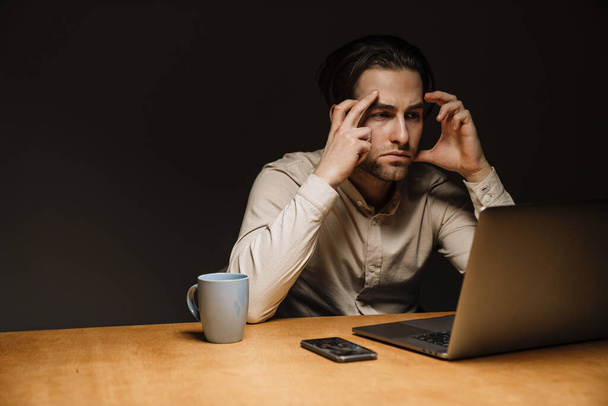 Serious pensive brunette businessman working on laptop computer in dark office - Foto, immagini