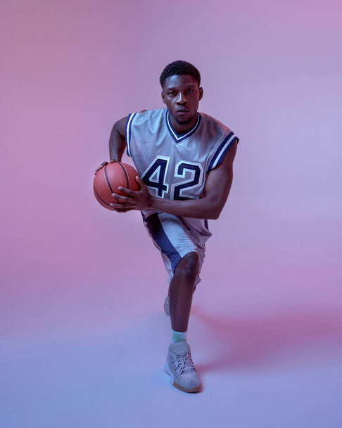 Basketball player practicing with ball in studio, neon background. Professional male baller in sportswear playing sport game. - Foto, immagini