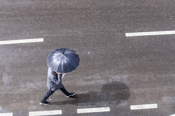 Una vista aérea de un macho sosteniendo un paraguas mientras camina por la calle - Foto, Imagen