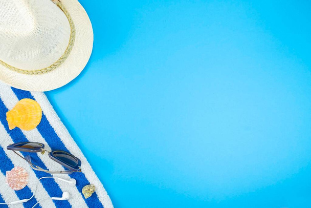 Letnie wakacje z ręcznikiem, kapeluszem, okularami przeciwsłonecznymi i zestawami słuchawkowymi na niebieskim tle. Odbiór, widok z góry - Zdjęcie, obraz