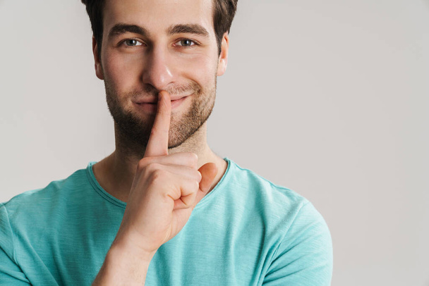 Smiling casual man with finger on lips keeping a secret isolated ovwe gray background, close up - Фото, зображення