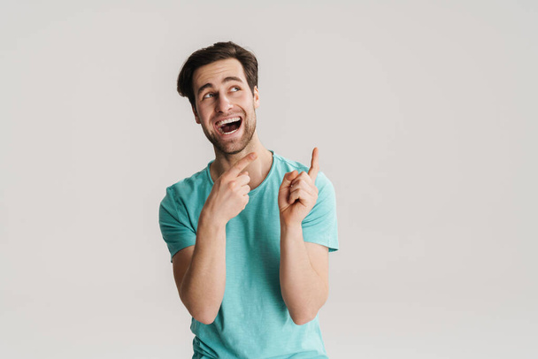 Joyful handsome guy laughing and pointing fingers upward isolated over white wall - Fotoğraf, Görsel