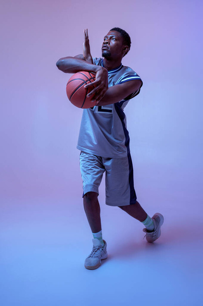 Strong basketball player hand holds ball in studio, neon background. Professional male baller in sportswear playing sport game. - Fotografie, Obrázek