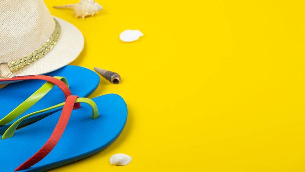 Blue flip-flops, hat and seashells on yellow background. Copy space - Φωτογραφία, εικόνα