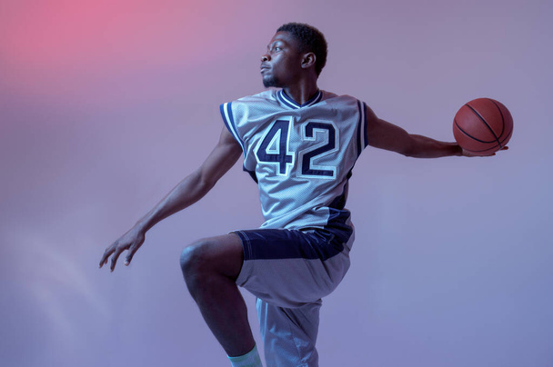 ボールを持つバスケットボール選手は、スタジオでの彼のスキルを示しています,アクションでジャンプ,ネオンの背景.スポーツウェアのプロの男性ボールスポーツゲーム,背の高いスポーツマン - 写真・画像