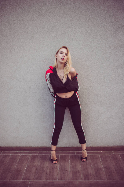 A portrait of a young sexy blonde female wearing a crop top with black sportswear and high heels - 写真・画像