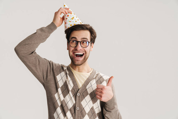Cheerful young man geek celebrating birthday isolated over gray background - Foto, Imagem