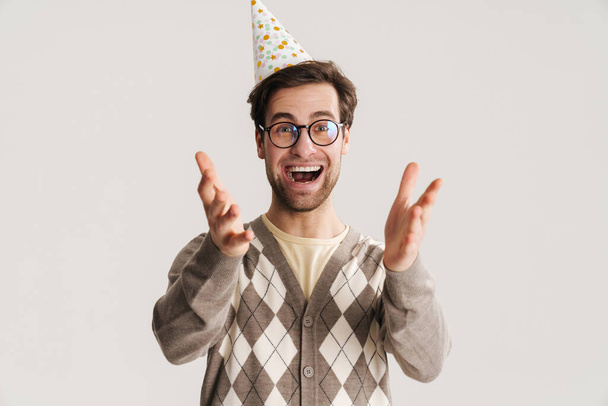 Cheerful young man geek celebrating birthday isolated over gray background - Photo, image