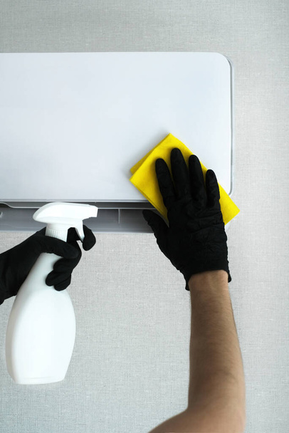 un hombre para limpiar el aire acondicionado en casa con guantes con una herramienta especial. empresa de limpieza para la limpieza. aire acondicionado limpieza maqueta - Foto, imagen
