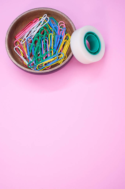 A vertical shot of multi-colored paper clips and duct tape on a pink surface - copy space - Fotó, kép