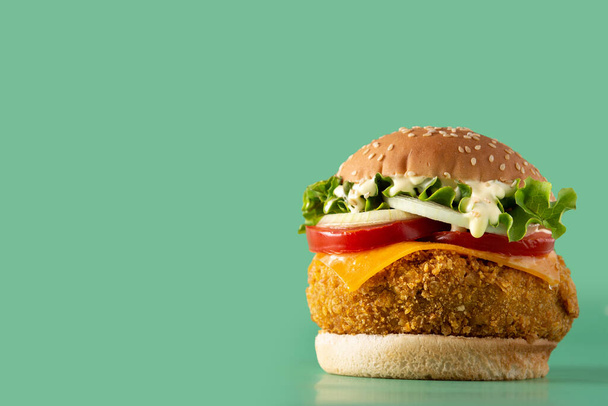Crispy kip hamburger met kaas op groene achtergrond - Foto, afbeelding