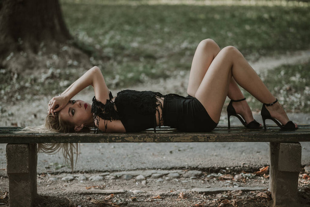 A sexy blonde female posing on a wooden bench in a park - Фото, зображення