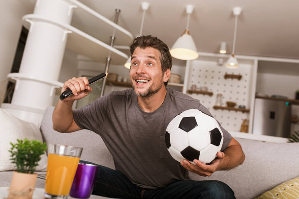Jonge voetbal fan man kijken naar voetbal wedstrijd op televisie in de woonkamer bank. - Foto, afbeelding