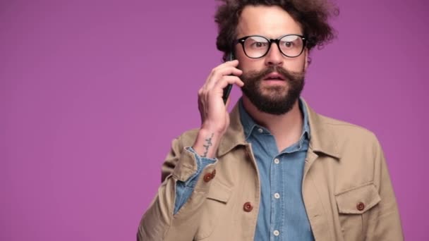 bearded young man in beige suit talking on the phone, smiling and nodding, having a good conversation, laughing, grimacing and gesturing on pink background in studio - Footage, Video