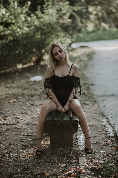 A sexy blonde female posing on a wooden bench in a park - Valokuva, kuva