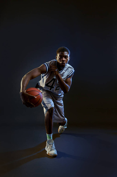 Kosárlabda játékos labdával, akció közben gyakorol a stúdióban, fekete háttérrel. Profi férfi játékos sportruházat játék sport játék, sportoló - Fotó, kép