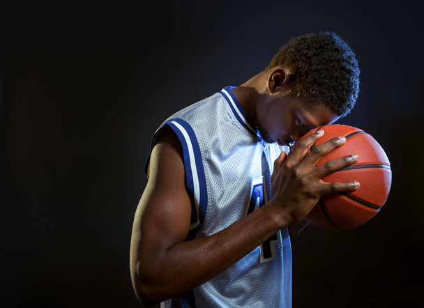 Zaostřený basketbalista pózuje s míčem ve studiu, černé pozadí. Profesionální mužský míč ve sportovním oblečení hrát sportovní hru, vysoký sportovec - Fotografie, Obrázek