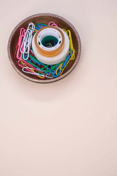 A vertical shot of multi-colored paper clips and duct tape on a beige surface - copy space - Fotó, kép