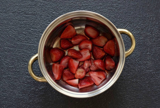 Cut the strawberries into halves or quarters. Transfer the strawberries to a pot of water, add sugar. - Photo, image