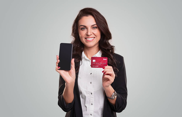 Cheerful businesswoman showing smartphone and credit card - Fotó, kép